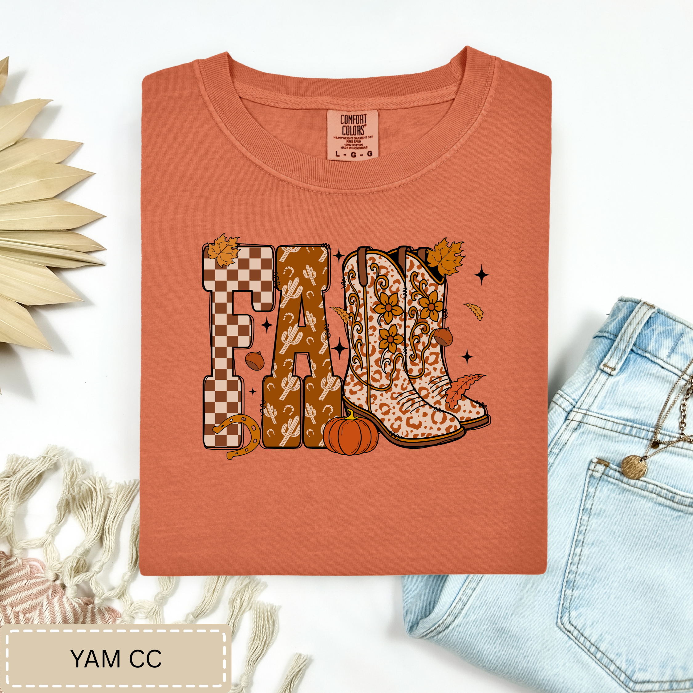 Folded orange t-shirt with autumn-themed design on a white background